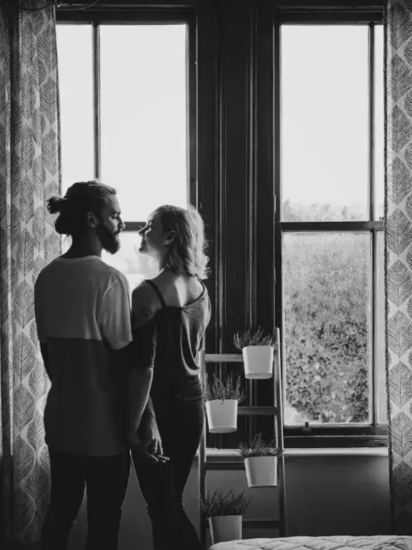 Sort-hvid foto af et par, der står foran et vindue og beregner deres huslån med en låneberegner.
