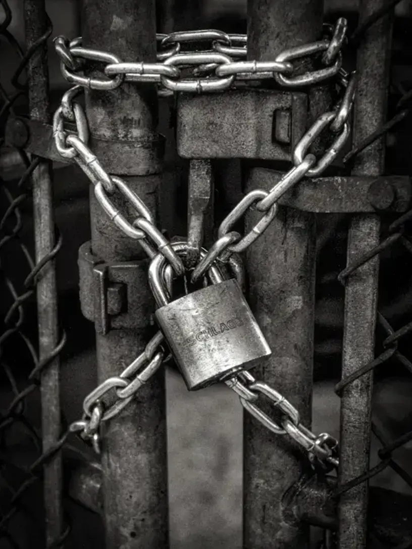 Et monokromt fotografi af en hængelås fastgjort på et kædehegn.