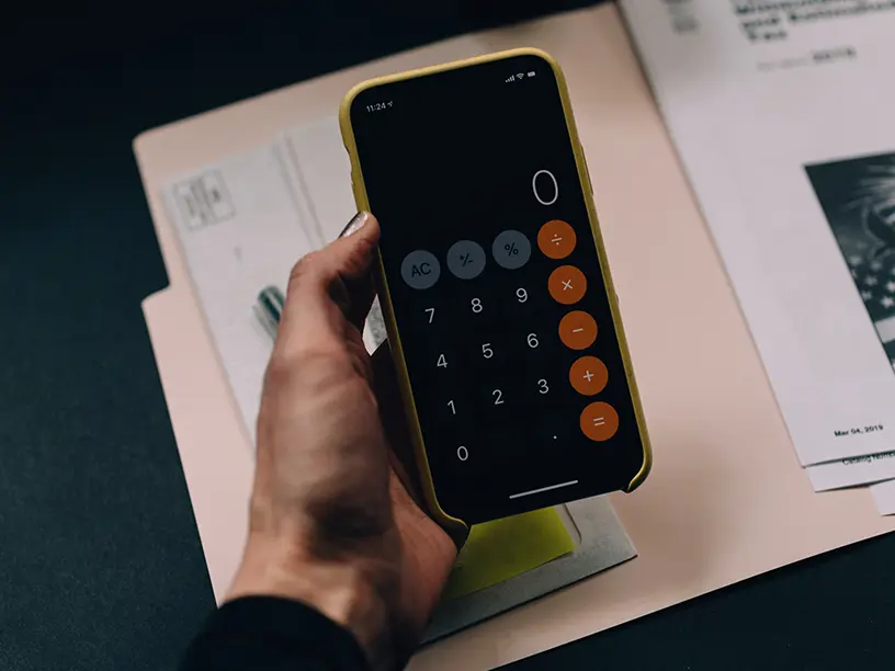 En person, der holder en telefon med en lommeregner på, og beregner deres rådighedsbeløb for 2023.