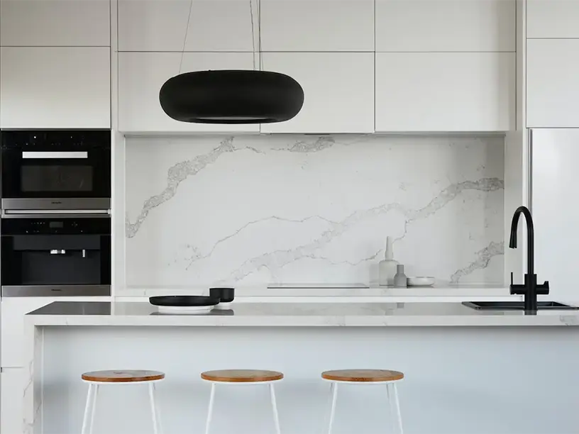 Et hvidt køkken med sorte taburetter og marmorbordplade med lån til sommerhus.