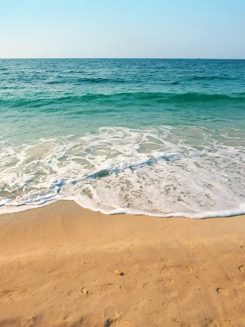 En solrig strand med bølger og sand.